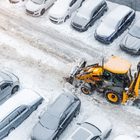 A snow plow clearing a residential parking lot during winter