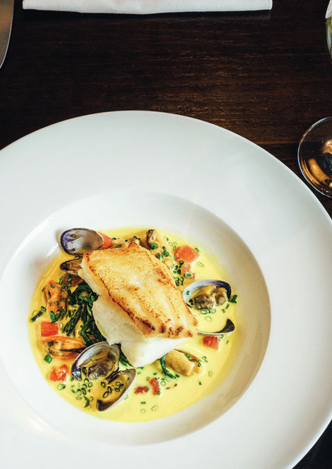 Plated fish and seafood dish with wine glass on a table.