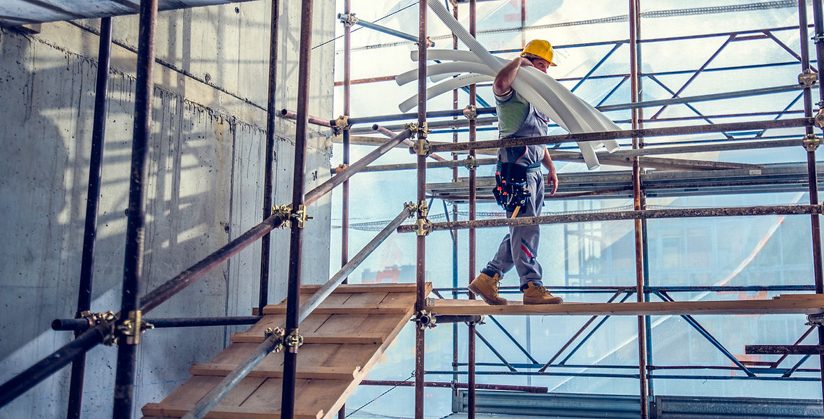 Construction worker carrying bunch of pipes on shoulder at construction site
