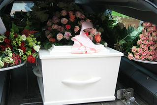 White coffin covered with flowers inside a grey hearse