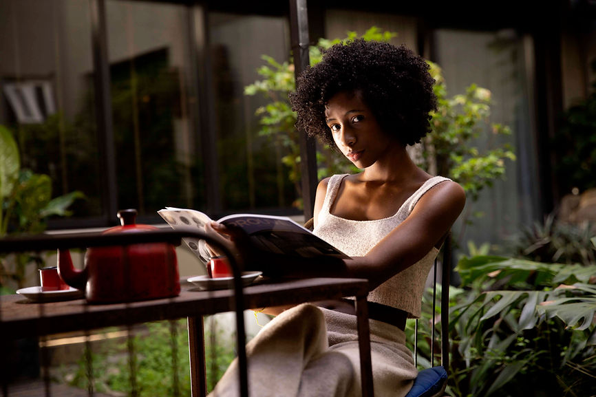 Girl looking up from reading a magazine in a café, surrounded by greenery and plants.