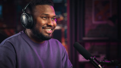 A black male podcaster wearing headphones with podcast mic