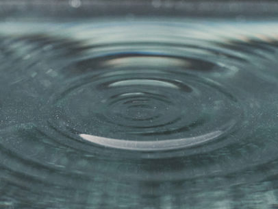 A close up image of calm blue water with gentle ripples expanding outward in soft circles, creating a sense of movement beneath a peaceful surface.