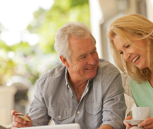 Smiling couple drinking coffee and shopping online on patio