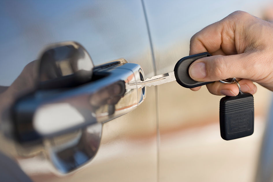Close-up of a hand inserting a metal car key into a silver vehicle door lock