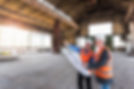workers discuss blueprints inside a large empty warehouse