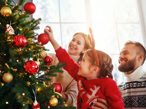Trois humains autour d'un sapin de noël décoré de boules rouges