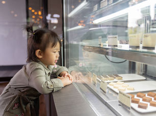 Une petite fille observe attentivement des pâtisseries derrière une vitrine, image évoquant le désir discret, l’hésitation et la retenue au cœur des différences culturelles entre le Japon et la France.