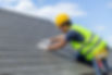 Roofer wearing a yellow hard hat and hi-vis vest inspecting roof tiles on a house in Newcastle-under-Lyme