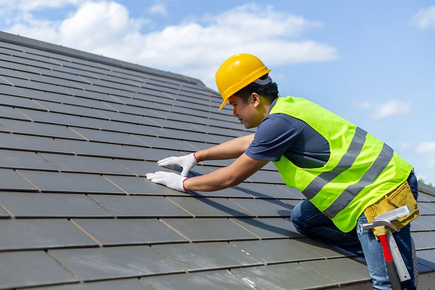 Roof repair, worker with white gloves replacing gray tiles or shingles on house with blue sky as background