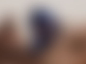 A man in blue turban amidst his camels looks directly at us.