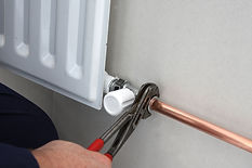 a person using pliers to tighten a connection on a copper pipe attached to a white central heating radiator valve