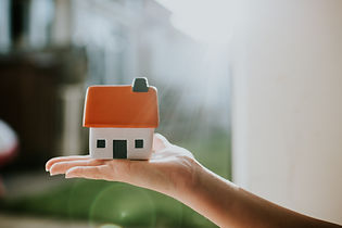 Person holding a small model house with a white base and grey roof in their palm