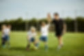 Male sports coach giving a high five to a young child playing football on a sunny green field