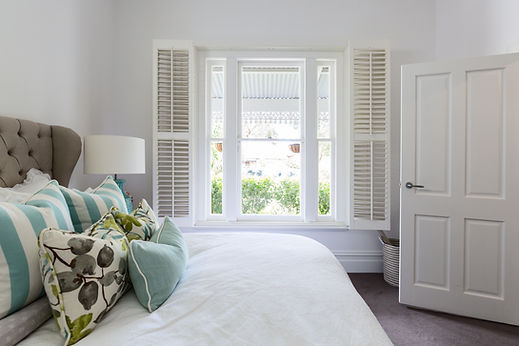 Elegant bedroom window fitted with bespoke white tracked shutters framing a beautifully made bed