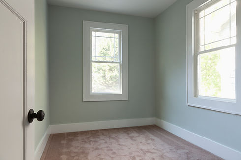 Small empty room with pale green walls, beige carpet, and windows