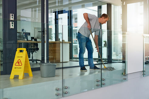 Man mops a modern office hallway with glass walls, sunlight streaming through