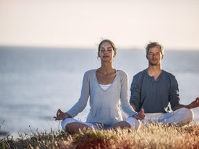 2 people meditating on a beach