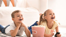Deux enfants riant regardent la télévision avec popcorn, outil d’immersion linguistique dès le plus jeune âge