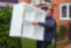 A person carries a white shelving unit outside a home with brick walls