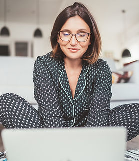 Mulher de óculos sentada em frente ao notebook, trabalhando no chão
