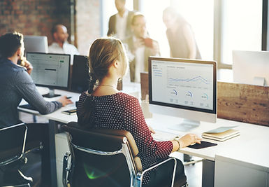 Office scene with people working at desks. Woman views data charts on monitor.