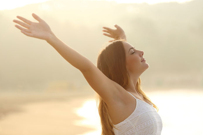A relaxed woman breathing fresh air raising arms at sunrise