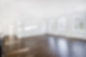 Spacious empty room with arched windows, white walls, and wooden floors