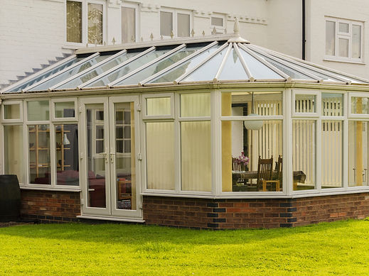 Large white multi panel Victorian style conservatory on a green lawn next to a white house
