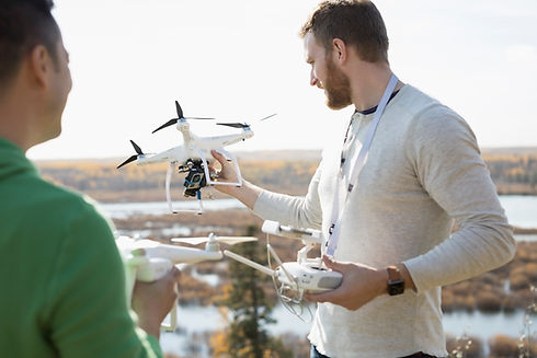 A man holding a drone and controller, with another man standing beside him