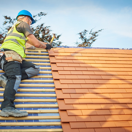 Builder in hard hat fixing terracotta tiles on a timber roof