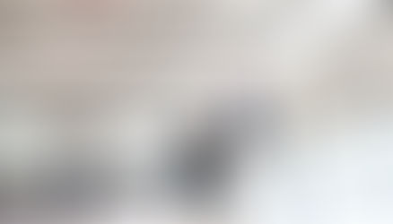 Sports hall with three basketball players. One person jumps to take a shot. Daylight floods the room, creating an energetic atmosphere.