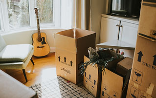 An acoustic guitar next to moving boxes in a sunlit room