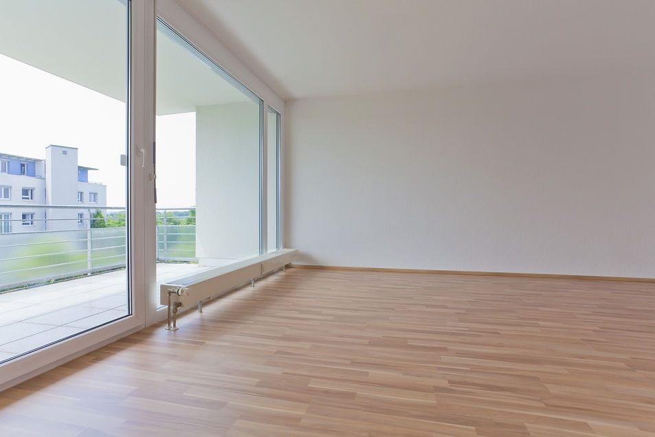 Modern empty room with light wood laminate flooring and large glass balcony doors