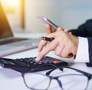 Person using a calculator with one hand while holding a phone in the other