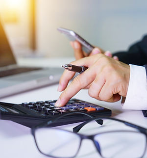 A person works at a desk using a calculator and smartphone, with a laptop open