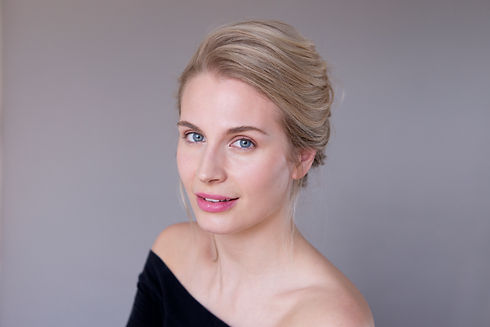 Portrait of a young blonde woman looking forward with natural makeup styling against a soft grey background