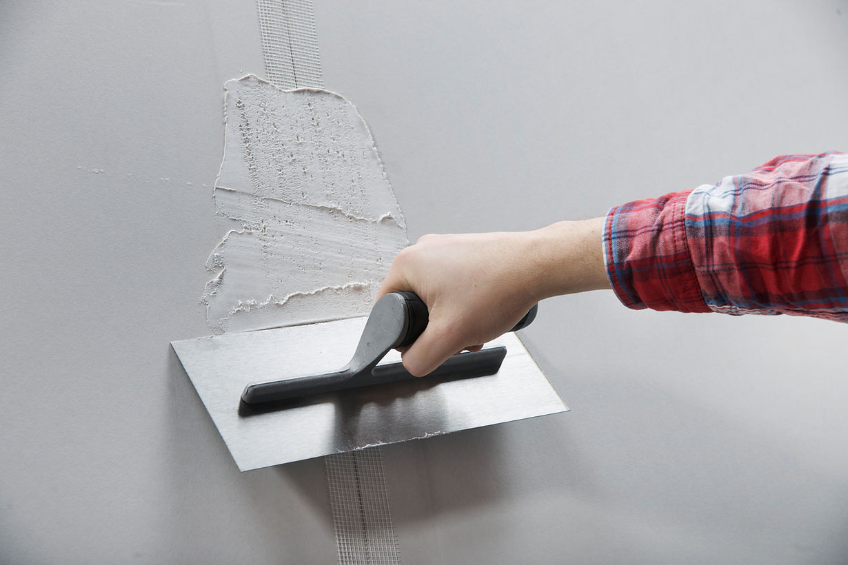A hand in a plaid shirt uses a trowel to apply plaster on a gray wall