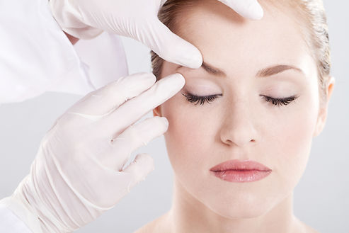 A person with closed eyes is gently touched on the forehead by gloved hands