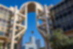 A modern building in Tel Aviv with a unique inverted pendulum design. The building is made of concrete and glass and features a large archway with a pendulum hanging from it.