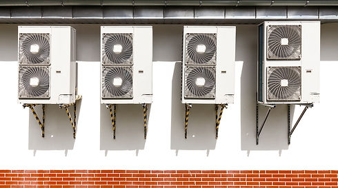 Four air conditioning units mounted on a white wall above a strip of red brick
