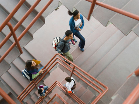 Students navigate a spiraling staircase, each holding books and backpacks, as they make their way through a campus building.