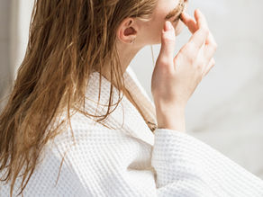 Close-up of a woman in a white robe applying a face mask in a bright bathroom, calm and focused.
