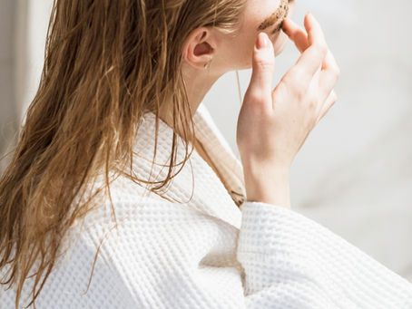 Close-up of a woman in a white robe applying a face mask in a bright bathroom, calm and focused.