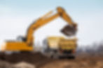 Yellow excavator loading dirt into a large dump truck at a construction site