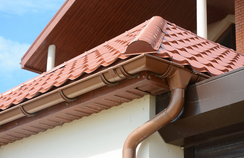 Close-up of brown corrugated metal roofing with matching brown plastic guttering and downpipe
