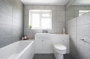A bathroom with grey tiles and white bathtub