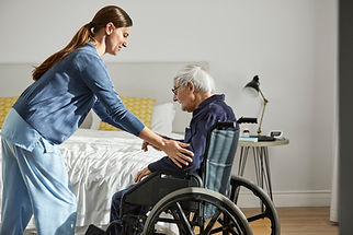 A female carer gently assisting an elderly man sitting in a wheelchair indoors
