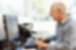 Elderly man typing on computer keyboard while looking at screen