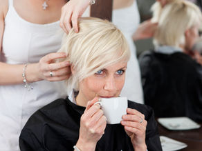 Frau sitzt beim Friseur mit Tasse in der Hand